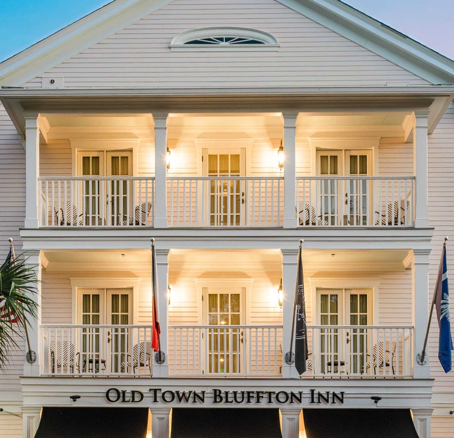 Old Town Bluffton Inn exterior featuring white colonial architecture with double-story balconies and warm evening lighting in Bluffton, South Carolina